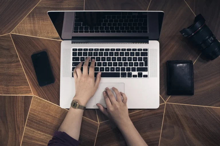 Mains sur le clavier d’un ordinateur portable posé sur un bureau en bois