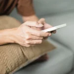Personne utilisant son smartphone allongée sur un canapé