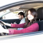 Élève conductrice au volant avec son moniteur d'auto-école qui prend des notes