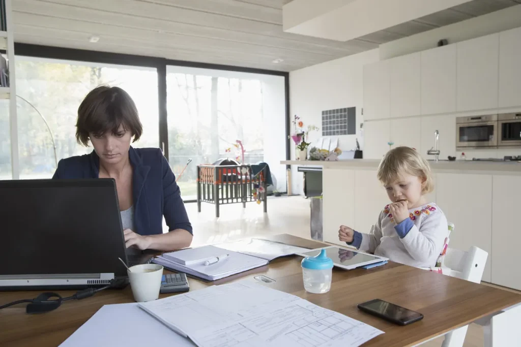 Mère faisant ses comptes à la maison pendant que son enfant joue, budget et pension alimentaire