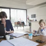 Mère faisant ses comptes à la maison pendant que son enfant joue, budget et pension alimentaire