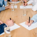 Mains de participants à une réunion autour d'une table en bois, négociation d'une convention collective