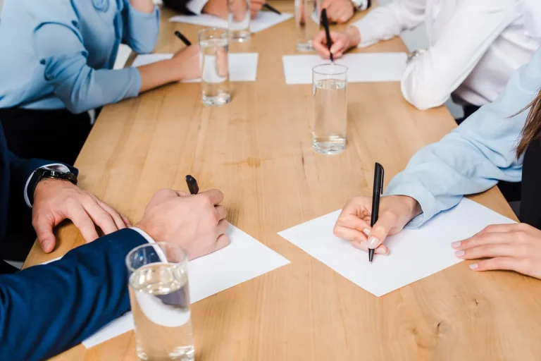 Mains de participants à une réunion autour d'une table en bois, négociation d'une convention collective