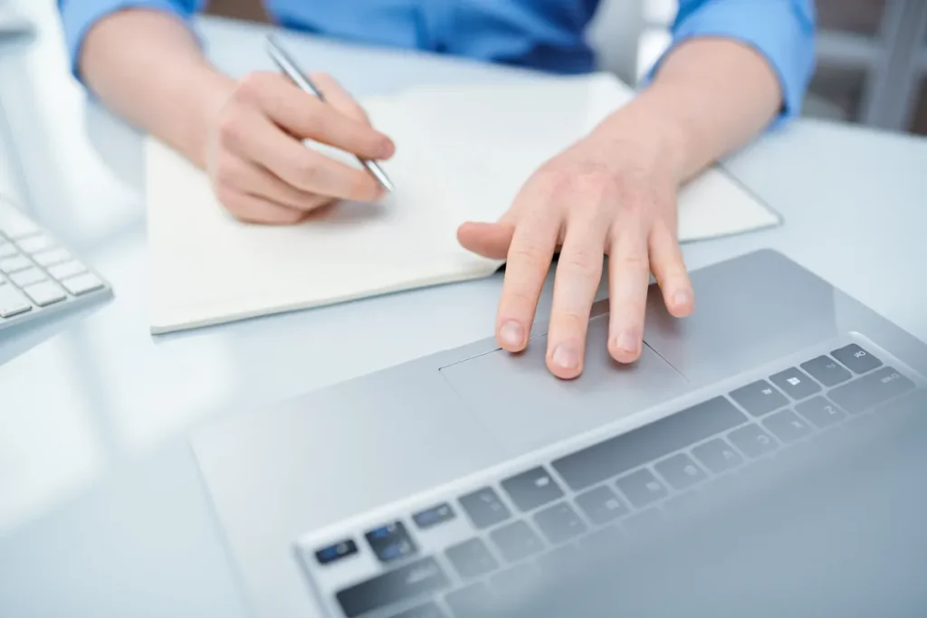 Mains sur un ordinateur portable et un carnet, démarches en ligne auprès de France Travail