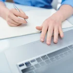 Mains sur un ordinateur portable et un carnet, démarches en ligne auprès de France Travail
