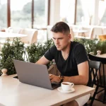 Jeune vacataire travaillant sur son ordinateur portable dans un café lumineux