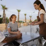 Jeune serveuse en job d'été servant un couple en terrasse