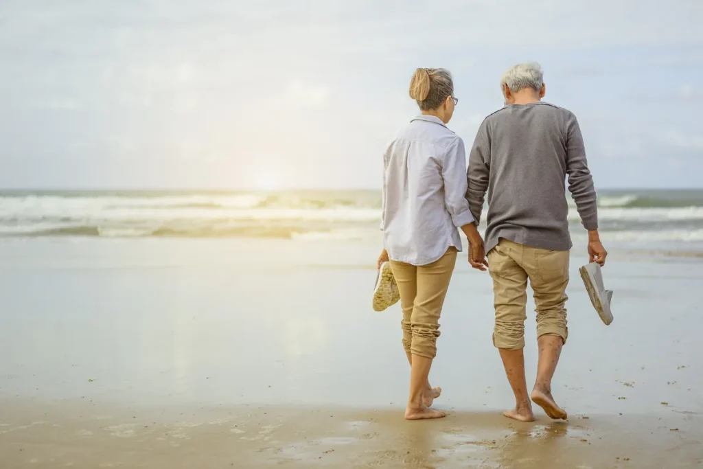 Couple de retraités marchant main dans la main sur une plage ensoleillée