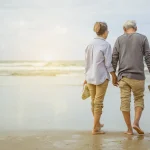Couple de retraités marchant main dans la main sur une plage ensoleillée