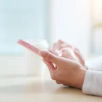 Mains tenant un smartphone rose près d'une fenêtre, utilisation d'un forfait mobile