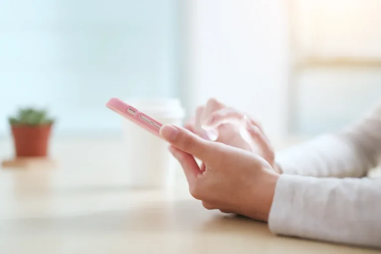 Mains tenant un smartphone rose près d'une fenêtre, utilisation d'un forfait mobile