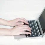 Mains tapant sur un ordinateur portable argenté pour réserver un nom de domaine